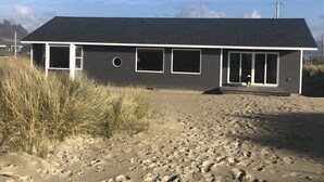 Ein modernes Strandhaus mit dunklem Dach, großen Fenstern und einer überdachten Eingangspforte.