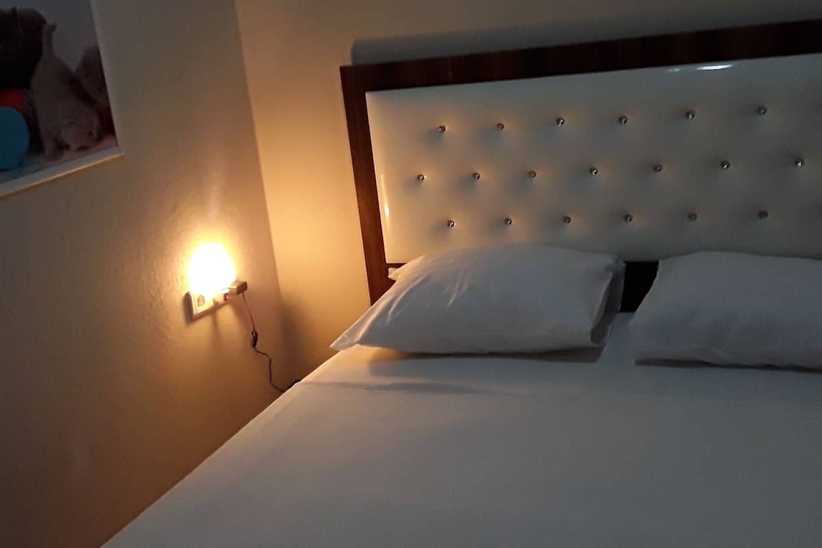 A bed with a tufted headboard, white bedding, and a wall-mounted light fixture.