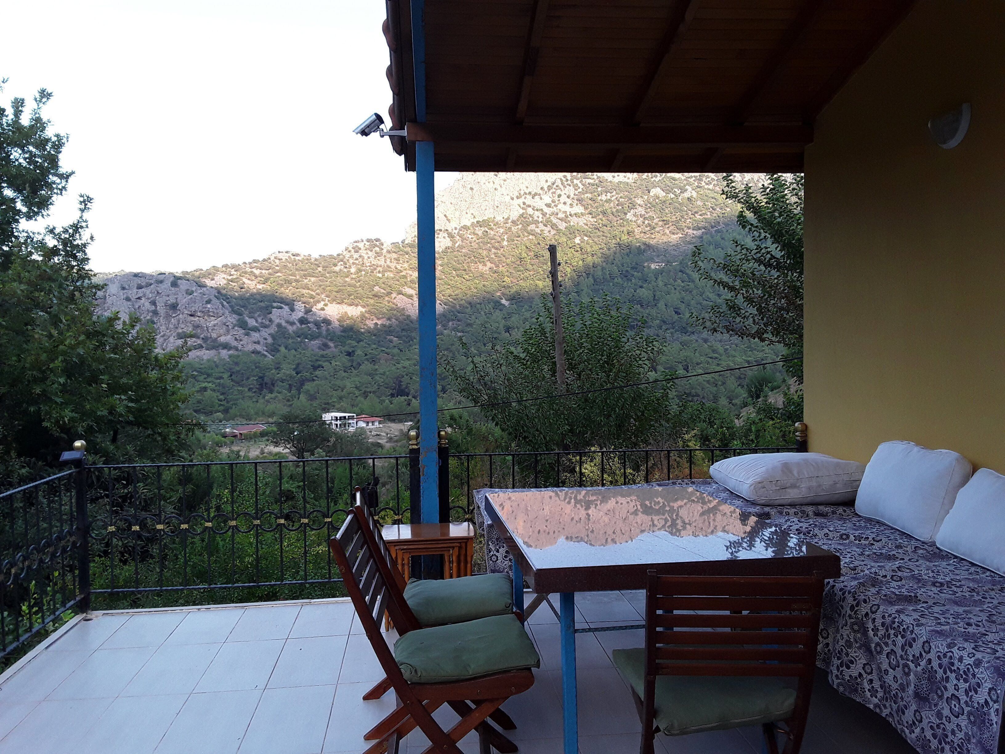 A balcony with a table and chairs, a sofa, and a view of a mountainous landscape.