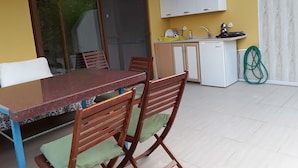 A dining area with a table and chairs, a kitchen with cabinets and a sink, and a sliding glass door leading to an outdoor area. - Waldvilla (Kumluca)