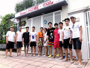 A group of people standing in front of a building with a sign that reads "Suna's HOME - Villa".