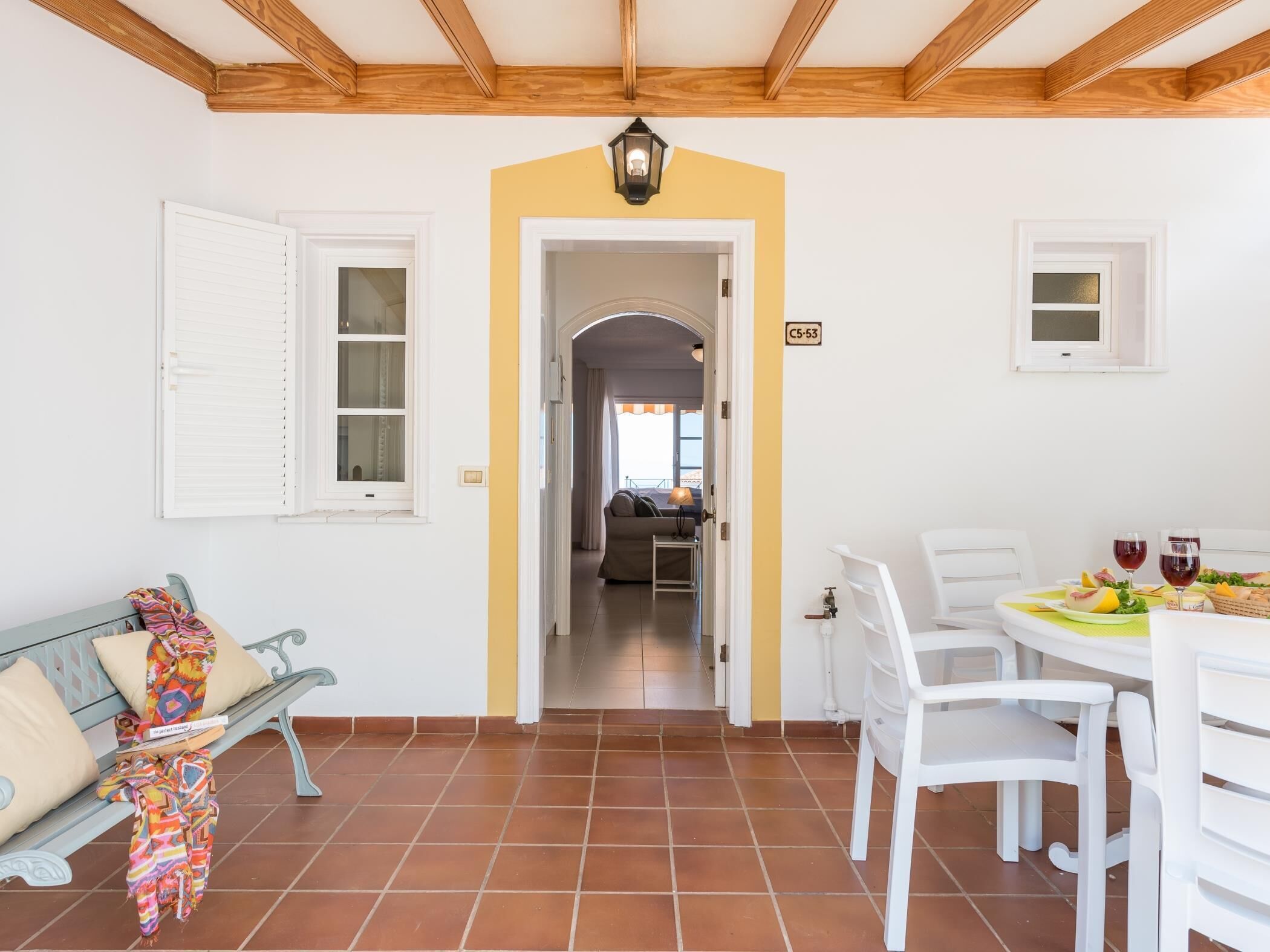 A room with a dining table set for two, a sofa, and a bench with colorful blankets.