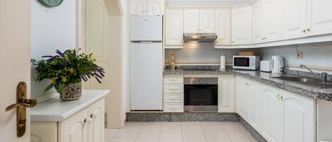 A modern kitchen with white cabinets, a built-in oven, a microwave, and a clock on the wall.