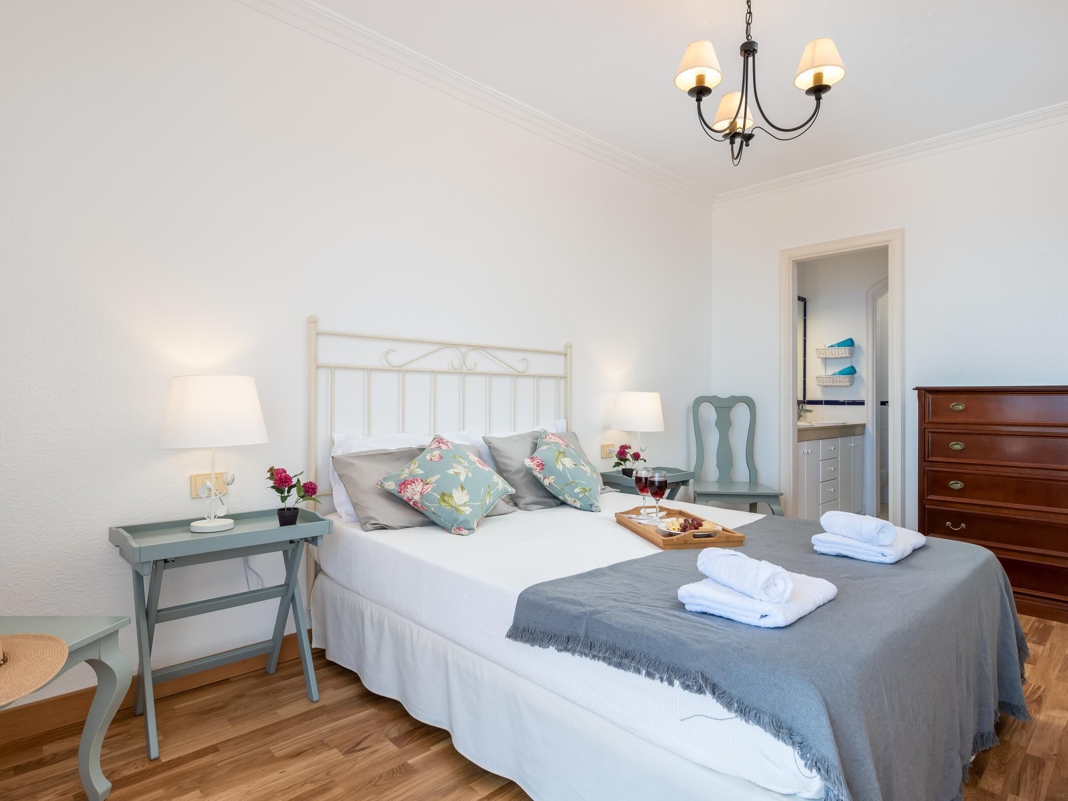 Une chambre à coucher bien rangée, avec un lit, des tables de chevet, une commode et un lustre.