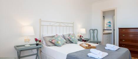 Une chambre à coucher bien rangée, avec un lit, des tables de chevet, une commode et un lustre.