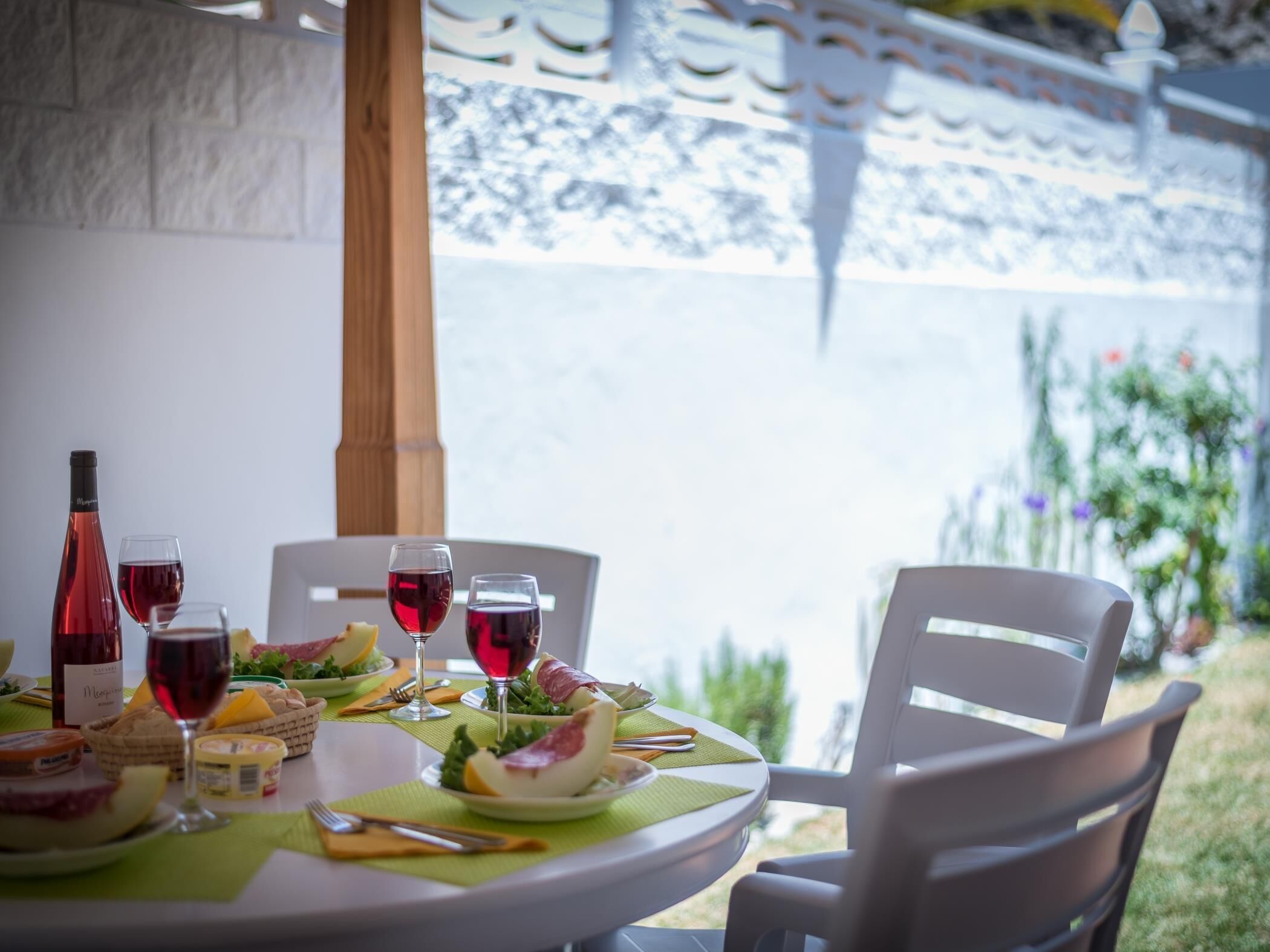 A round table set for a meal with plates, glasses, and a bottle of red wine.