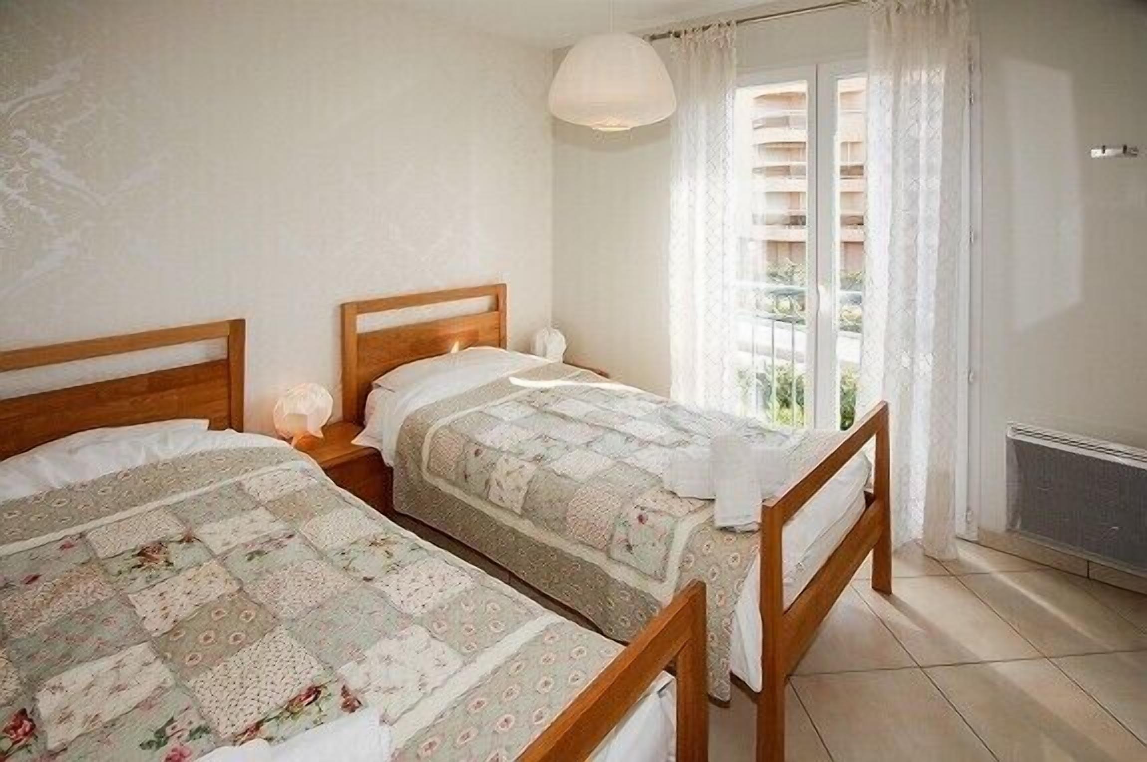 Un dormitorio con dos camas de madera, una ventana con cortinas y un radiador.