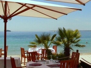 An outdoor dining area with tables and chairs, overlooking a beach and the sea.