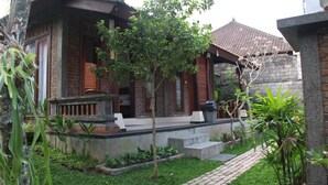 A traditional wooden house with a tiled roof, a small porch, and a garden with various plants and a pathway. - Ary House Ubud (Ubud)