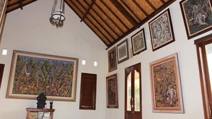 A room with a high wooden ceiling, multiple framed artworks on the walls, and a large painting on the left. - Ary House Ubud (Ubud)