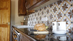 A kitchen with wooden cabinets, a tiled backsplash, and a loaf of bread on a cutting board. - Dingle Town House 3 bedroom house VRBO (Dingle Peninsula)