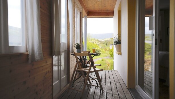 A wooden deck with a table and chairs, a potted plant, and a view of greenery. - Dingle Town House 3 bedroom house VRBO (Dingle Peninsula)