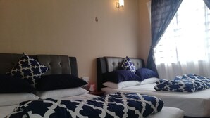 Habitación de hotel con dos camas, cada una con cabecero y varios almohadones. Se ve una mesita de noche con una lámpara y una caja de pañuelos.