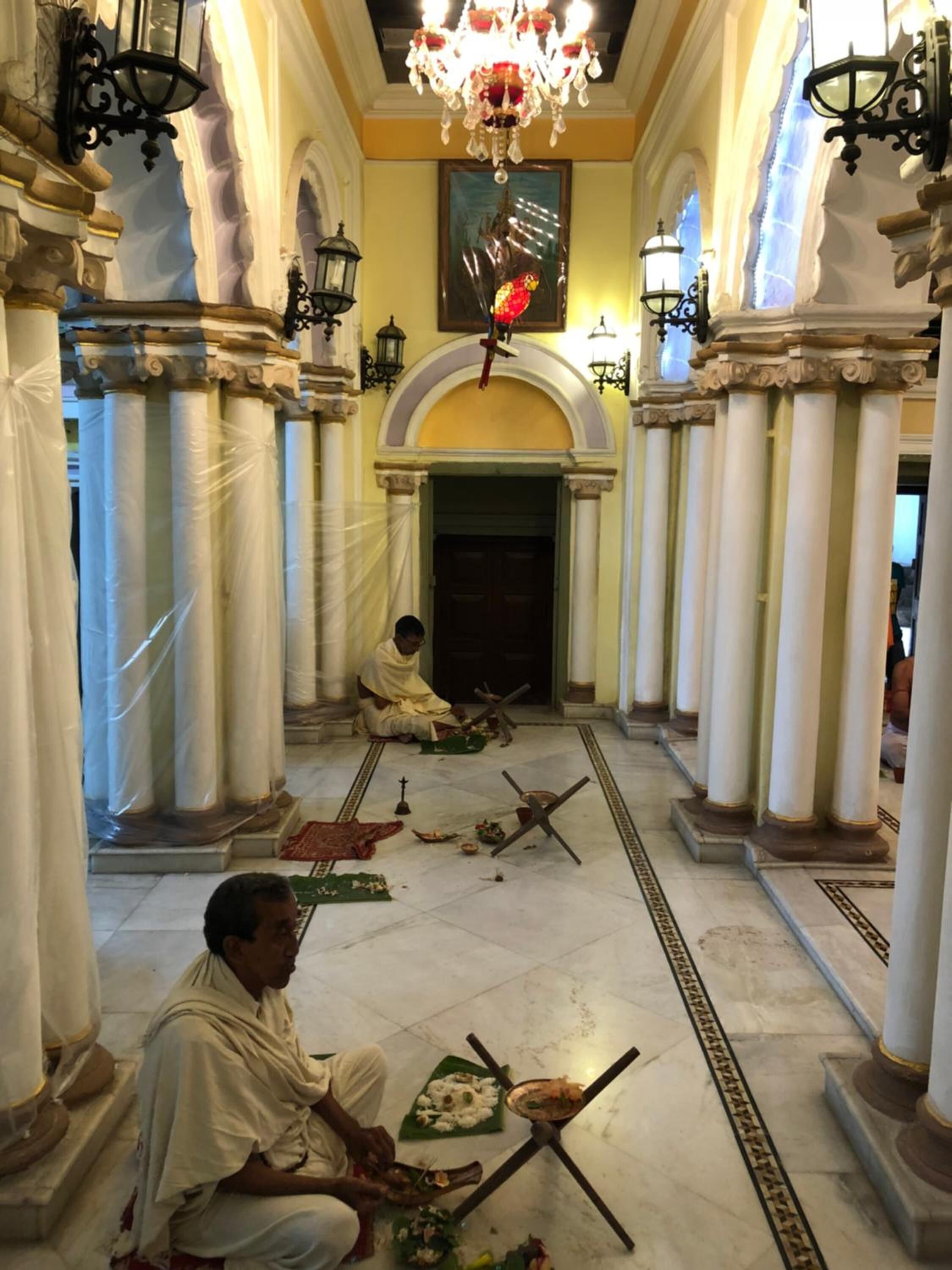 A corridor with columns, chandeliers, and a person performing a ritual.