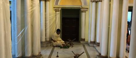 A corridor with columns, chandeliers, and a person performing a ritual.