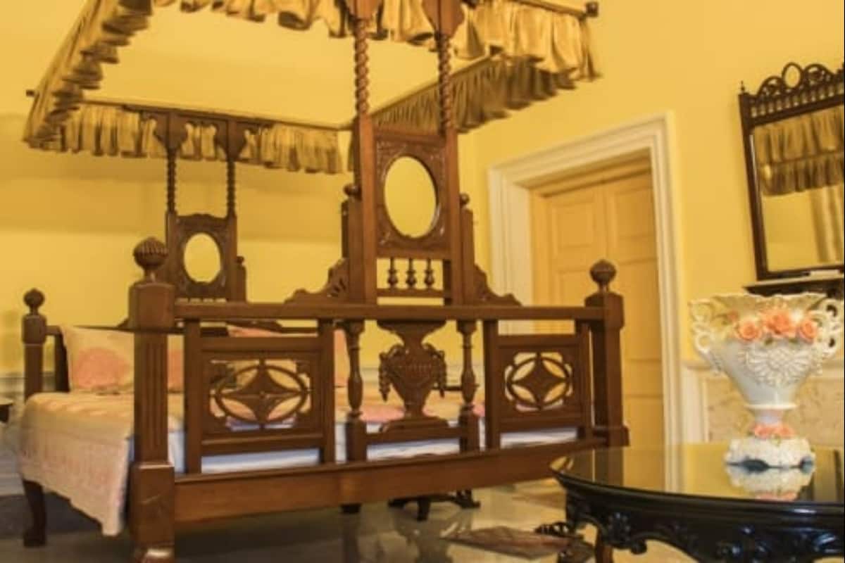 A traditional wooden bed with a canopy, a mirror, and a vase with flowers on a table.