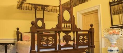A traditional wooden bed with a canopy, a mirror, and a vase with flowers on a table.