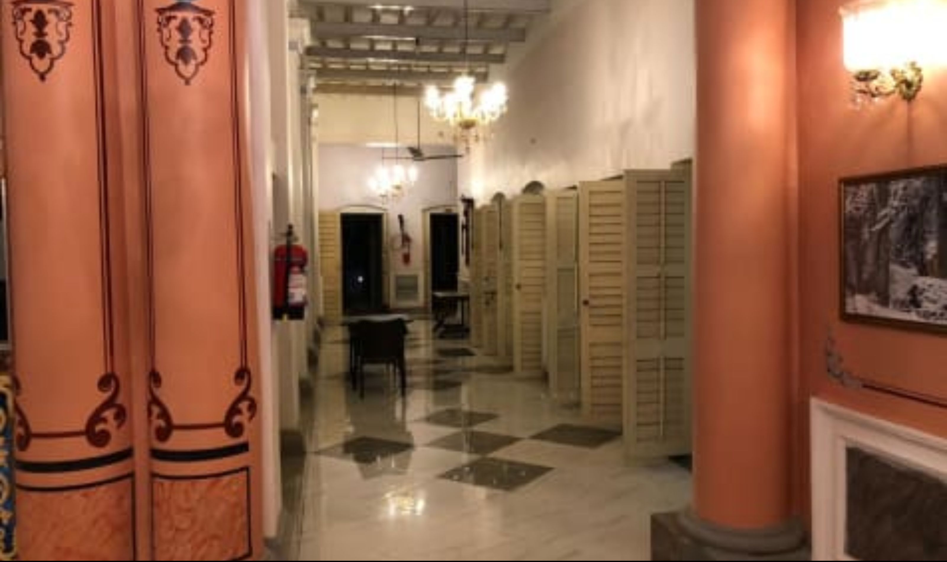A hotel corridor with a checkered floor, a row of lockers, and a chandelier.