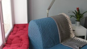 Ein Zimmer mit einem blauen Sofa, einer roten Bank, einer weißen Lampe und einer Pflanze.
