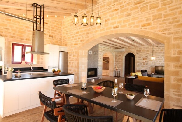A modern kitchen with a stone wall, a dining area with a table set for two, and a cozy living space with a sofa and fireplace.