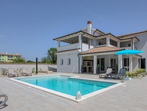 Ein zweistöckiges Haus mit Swimmingpool, Sitzgelegenheiten im Freien und einer überdachten Terrasse.