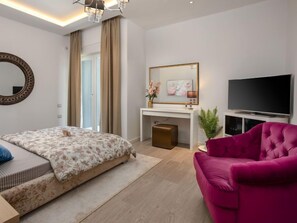 Ein modernes Schlafzimmer mit Bett, einem rosafarbenen Sofa, einem Fernseher und einem Schreibtisch mit Spiegel und Kunstwerken.