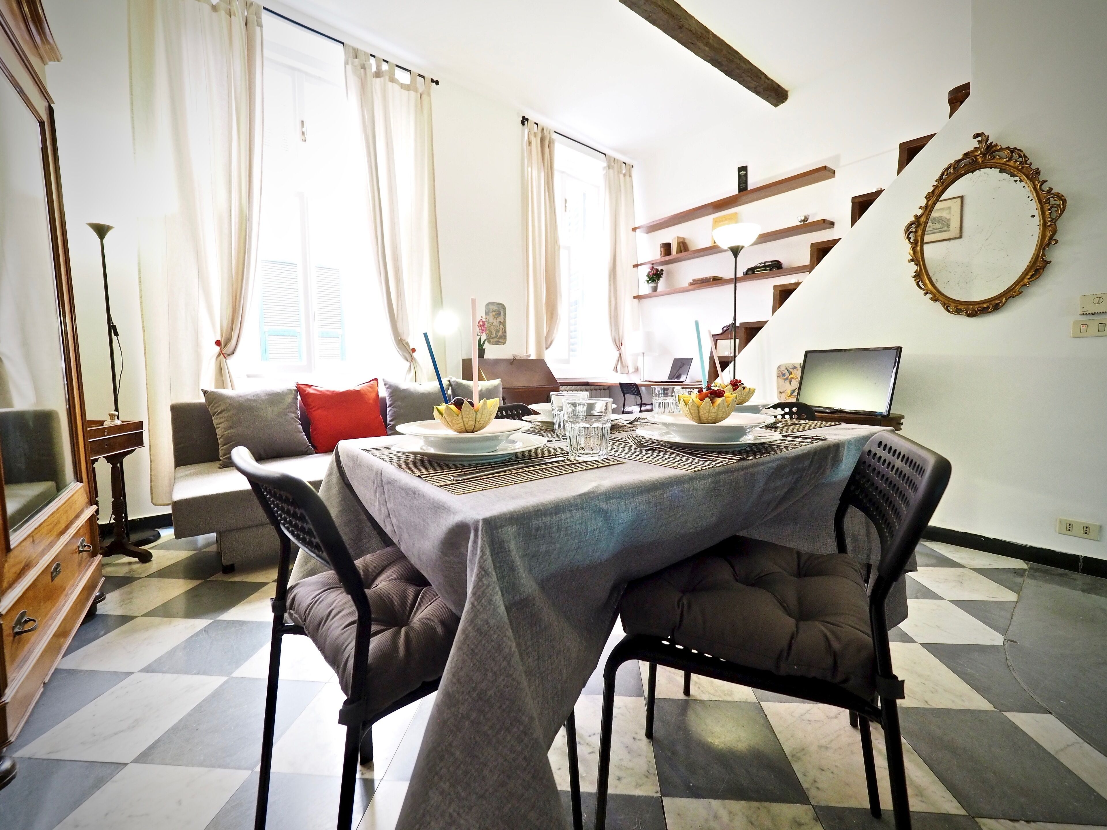 A dining area with a checkered floor, a table set with plates, glasses, and a laptop.