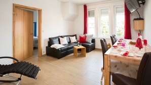 Ein Wohnzimmer mit einer schwarzen Couch, einem Esstisch für zwei Personen und einem Holzstuhl.