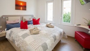 Ein Schlafzimmer mit Bett, Kissen, einem Nachttisch, einem Fenster und einem an der Wand befestigten Fernseher.