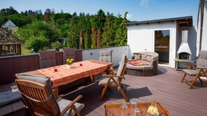 Eine Holzterrasse mit Tisch, Stühlen und einer gemütlichen Sitzecke, sowie ein Schornstein.