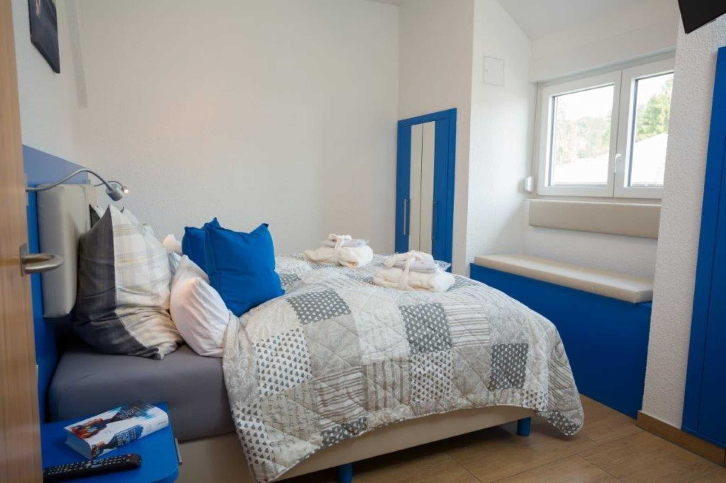 Ein Schlafzimmer mit einem Bett, einem Fenster, einem Nachttisch und einer blauen Wand.