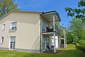 Um edifício de dois andares com varanda no andar superior, área de estar coberta ao ar livre e um gramado.