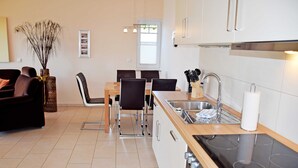 A modern kitchen with a dining area, featuring a stove, sink, and chairs. - Vacation apartment Ostseebad Göhren with great lake view - Ferienwohnung Ostseebad (Göhren)