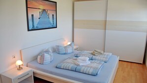 A neatly arranged bedroom with a bed, pillows, a bedside table with a lamp, and a painting on the wall. - Vacation apartment Ostseebad Göhren with great lake view - Ferienwohnung Ostseebad (Göhren)