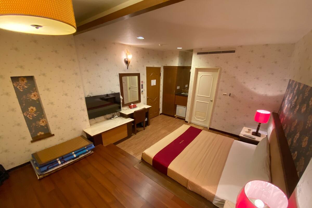 A bedroom with a bed, a desk, a mirror, a wardrobe, and a bathroom.
