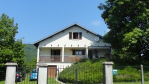 Une maison à deux étages dotée d’un balcon, d’une antenne parabolique et d’une allée pavée menant à une entrée fermée par un portail.