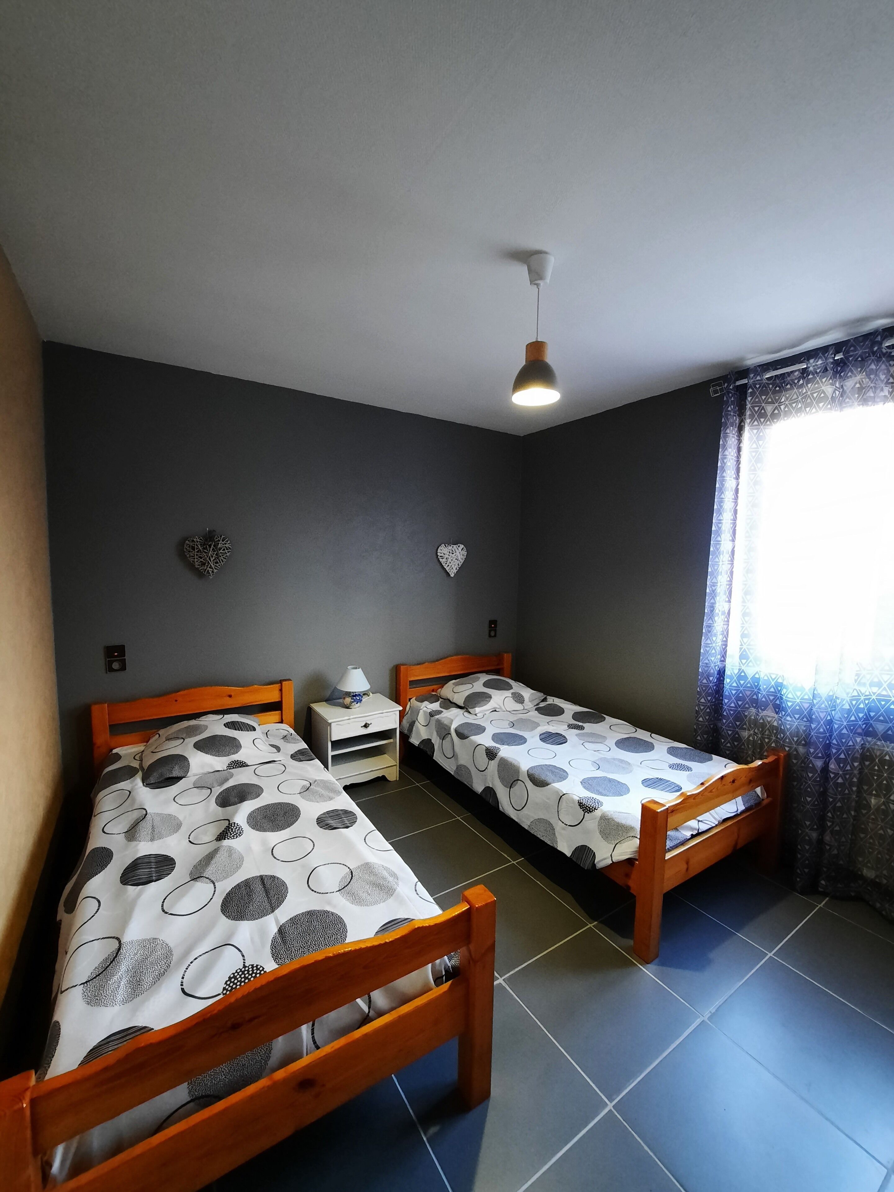 Une chambre avec deux lits en bois, une table de chevet avec une lampe et un luminaire au plafond.