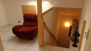 Une petite pièce carrelée, avec une chaise rouge, un escalier en bois et une lucarne.