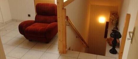 Una habitación pequeña con baldosas, una silla roja, una escalera de madera y un tragaluz.