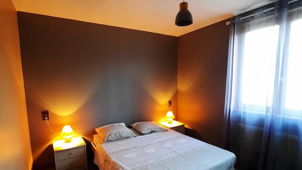 Une chambre à coucher avec un lit, deux tables de chevet avec des lampes, un luminaire au plafond et une fenêtre avec des rideaux.