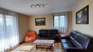 Un salon avec un canapé en cuir noir, une petite table et un fauteuil. Il y a un tableau au mur et un luminaire au plafond.
