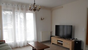 A living room with a wooden coffee table, two patterned armchairs, a television on a wooden stand, and a radiator on the wall. - Close to town center, many shops within walking distance (Revel)