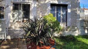 A stone building with two windows and a door, surrounded by a garden with mulch and plants. - Close to town center, many shops within walking distance (Revel)