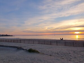 Une plage avec une clôture en bois et un coucher de soleil en arrière-plan.