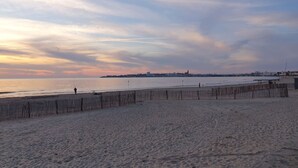Ein Strand mit einer Holzzaun, ruhigem Wasser und einer entfernten Skyline der Stadt.