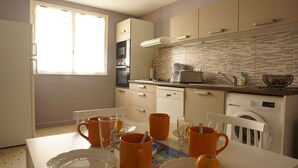 Eine moderne Küche mit weißen Schränken, einer gefliesten Spritzschutzwand und einem Essbereich mit orangefarbenen Tassen und Tellern.