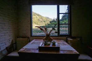 Ein Zimmer mit einem großen Fenster, einem Holztisch mit einer Vase und Teetassen, und einer Ziegelwand.