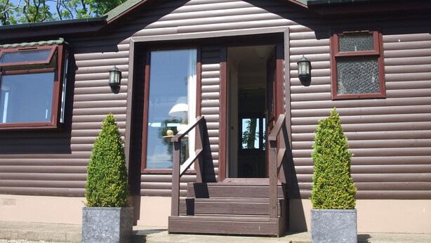 Una baita di legno con una porta d'ingresso, un piccolo portico e due vasi con piante.