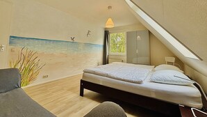 A bedroom with a bed, a hanging light, a window, and a beach mural on the wall.