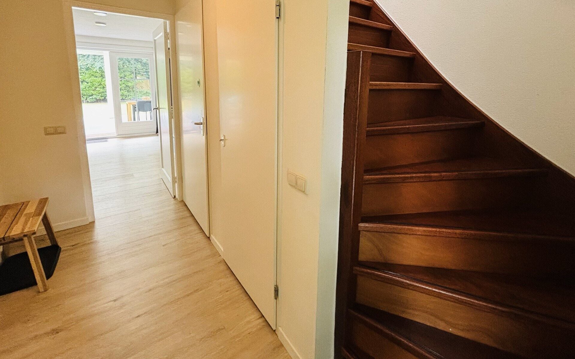 A wooden staircase leading to a landing with a bench and a door.